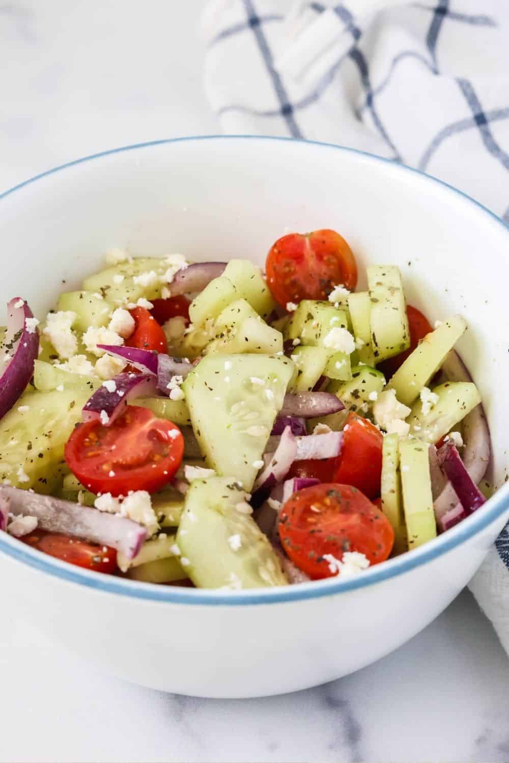 white bowl of cucumber salad with feta cheese and tomatoes.