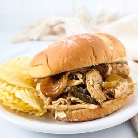 Dill pickle chicken served on a bun, placed on a white plate with potato chips on the side.