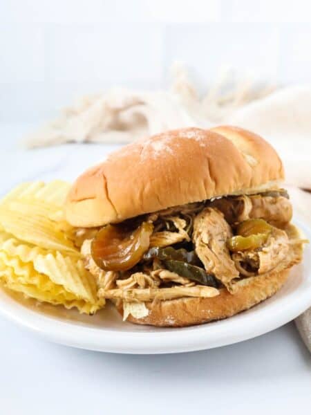 Dill pickle chicken served on a bun, placed on a white plate with potato chips on the side.