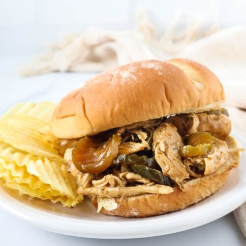 Dill pickle chicken served on a bun, placed on a white plate with potato chips on the side.