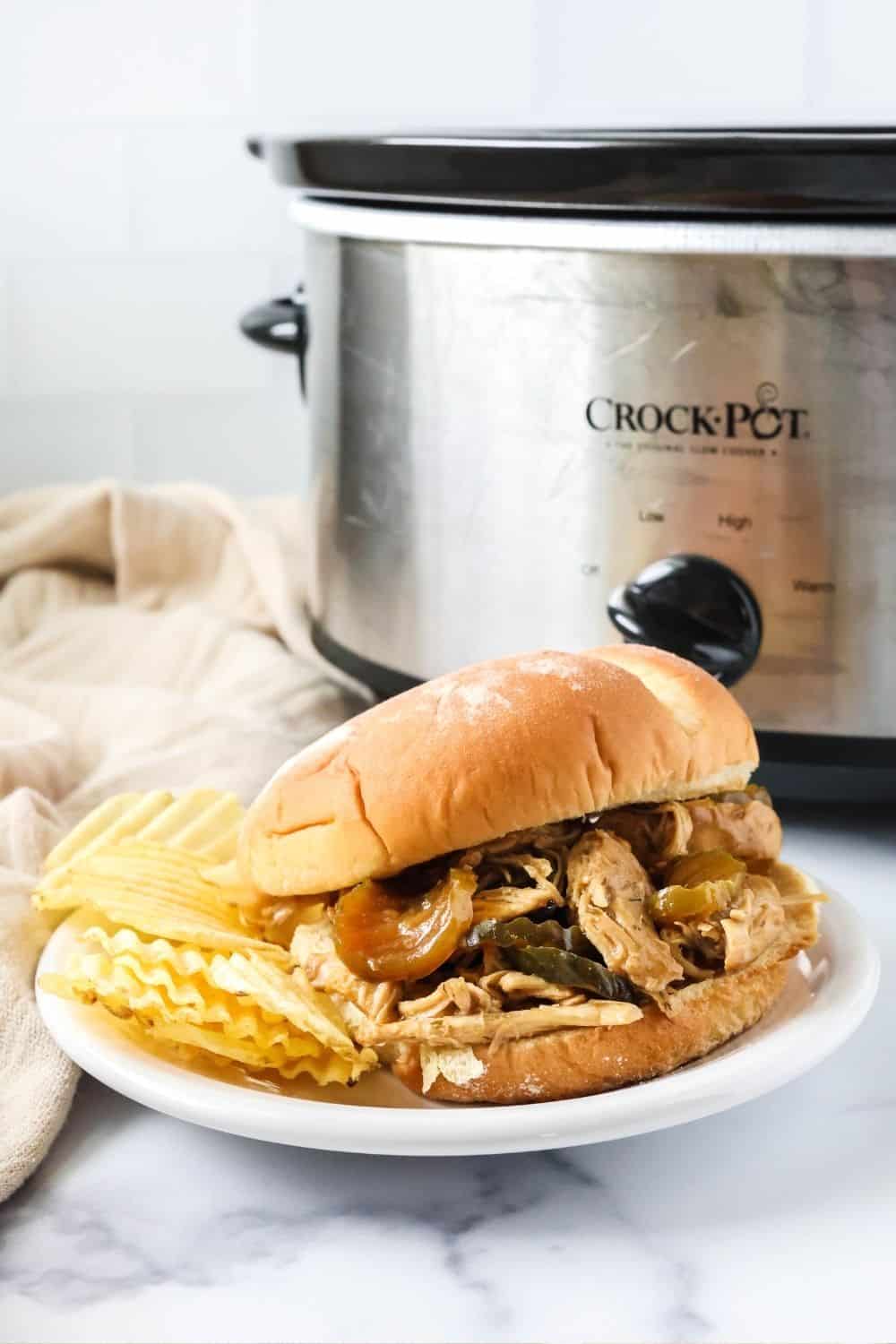 dill pickle chicken sandwich and potato chips on a white plate in front of a Crock Pot.
