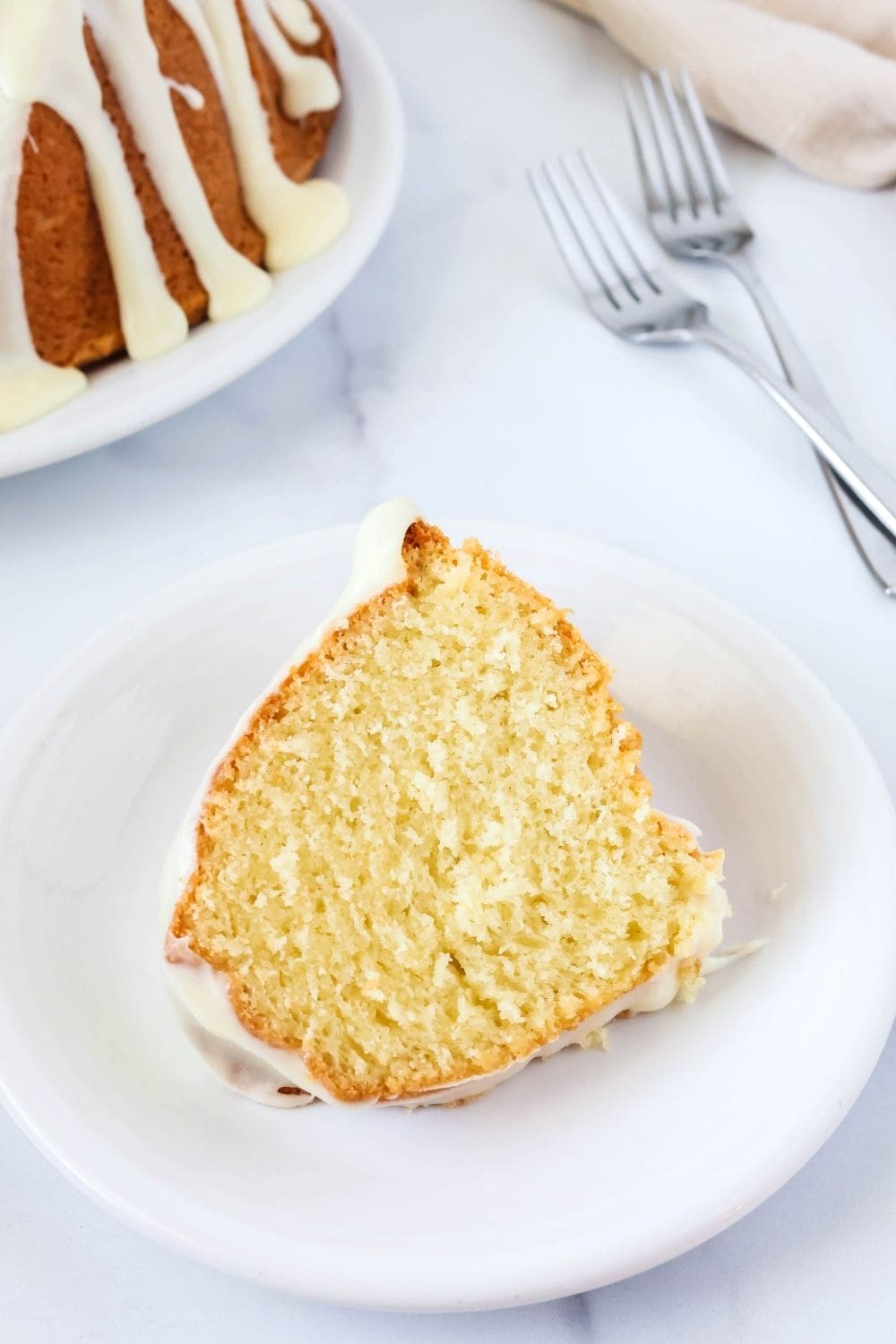slice of easy coconut pound cake served on a white plate, with two forks and the remainder of the bundt cake in the background.