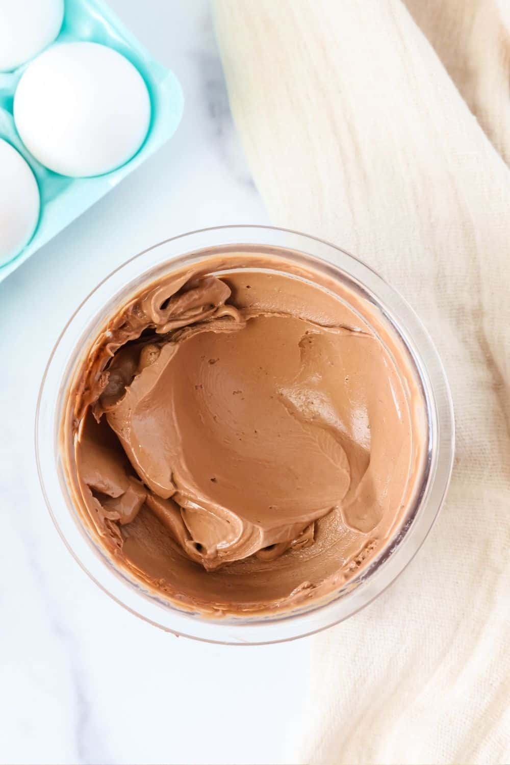overhead view of hard boiled egg pudding ice cream in a pint container, with a carton of eggs next to it.