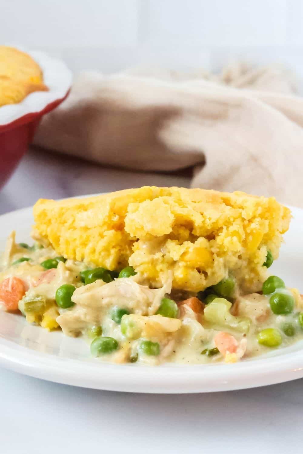 close-up side view of Jiffy cornbread pot pie serving on a white plate, showing the creamy filling and cornbread on top.