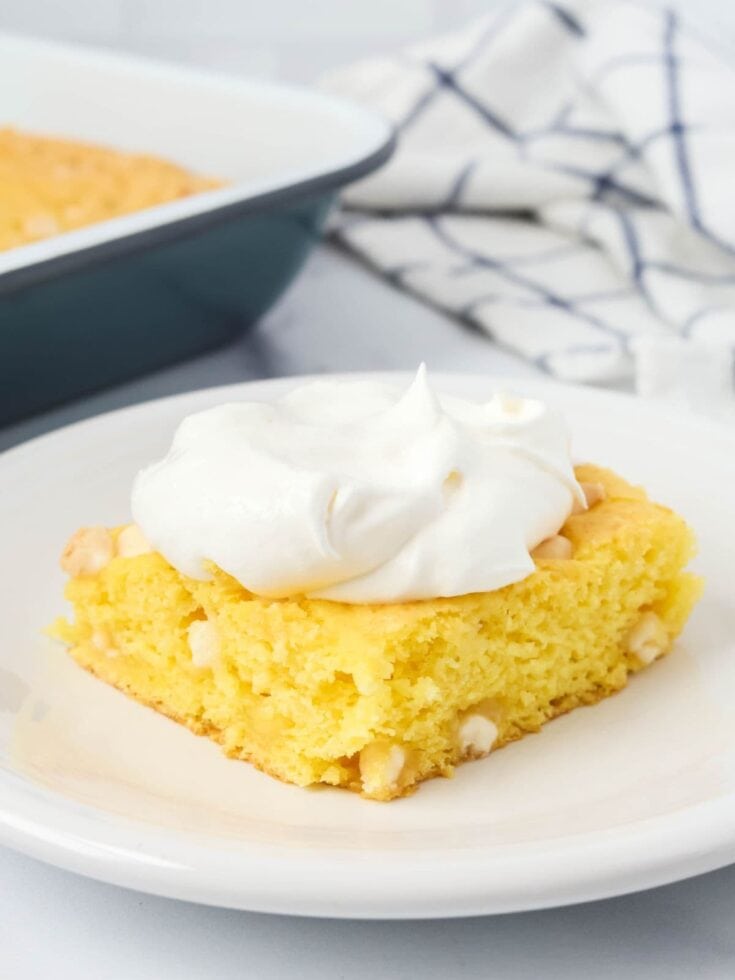 Slice of lemon pudding dump cake served on a white plate, garnished with whipped topping.