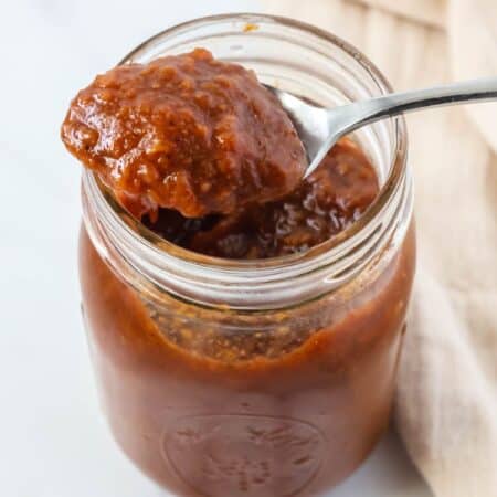 a spoonful of peach butter rests on the top of a jar of the fruit butter.