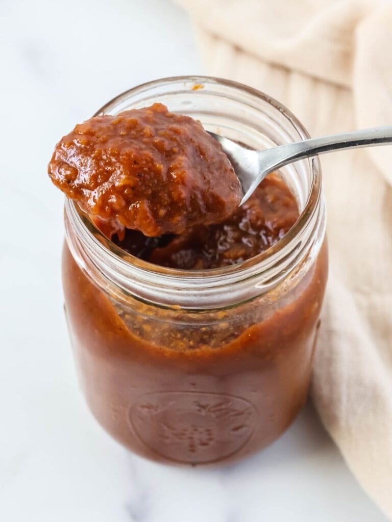a spoonful of peach butter rests on the top of a jar of the fruit butter.