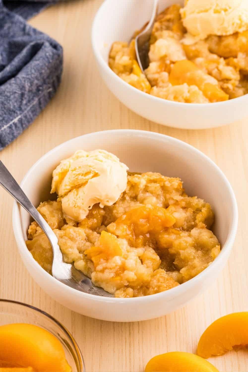 Two white bowls filled with servings of peach cobbler made with canned peaches and cake mix.