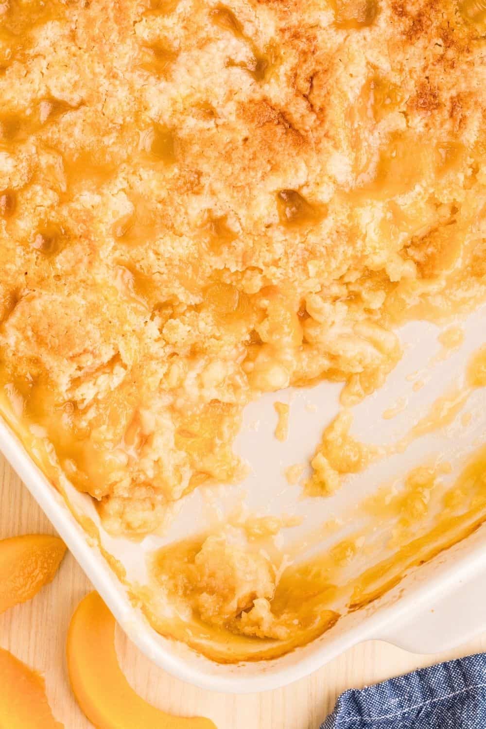 overhead view of a white baking dish of peach dump cake, with some of the dump cake scooped out of the dish.