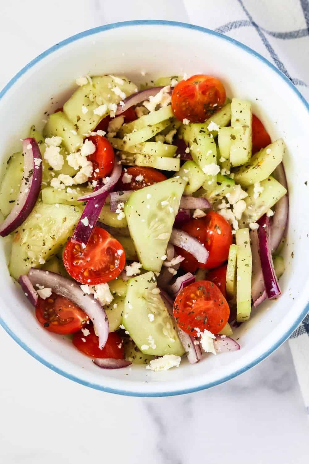 Summer cucumber tomato onion salad served in a white bowl.