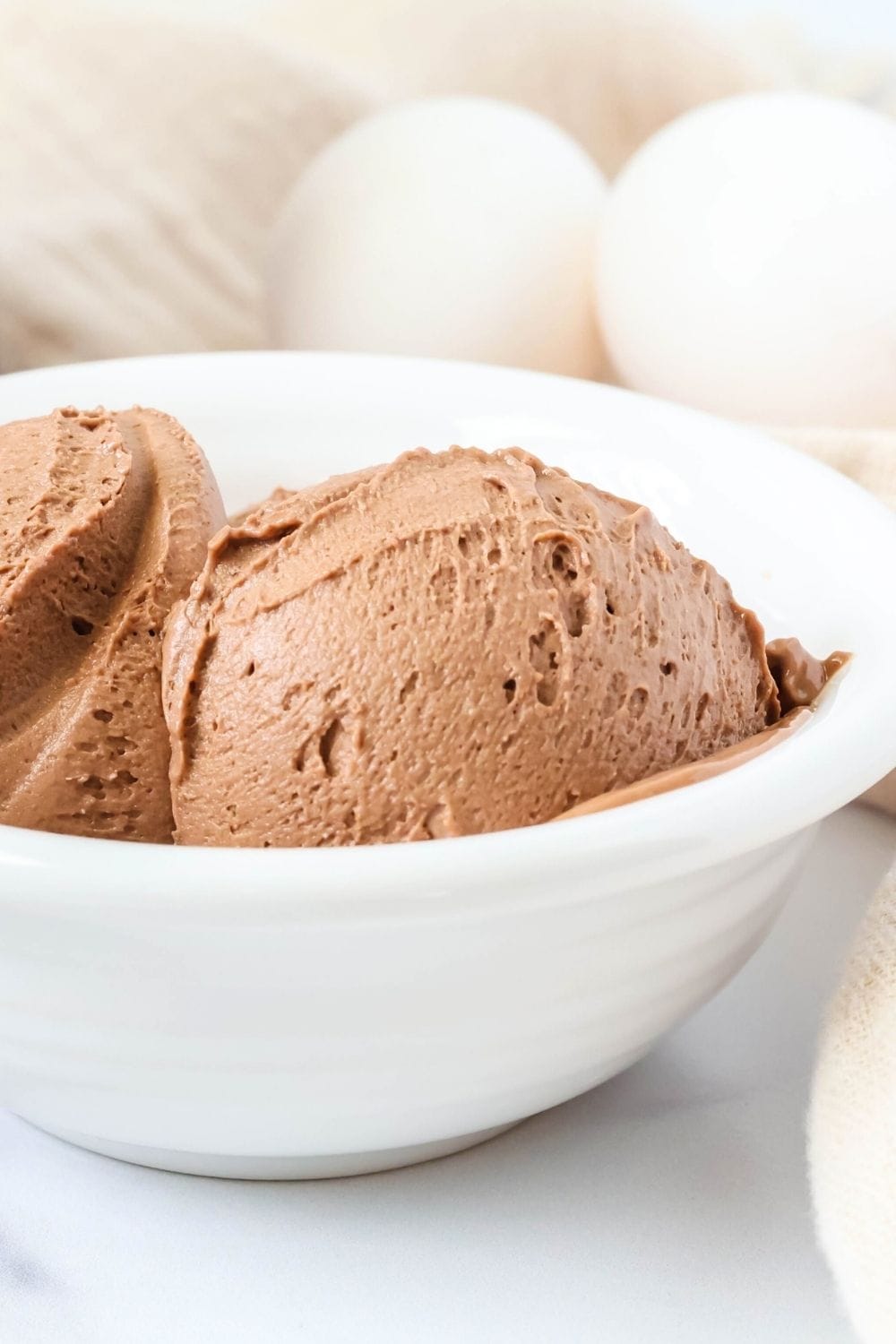close-up side view of scoops of smooth and creamy chocolate ice cream made from boiled eggs, served in a white bowl.