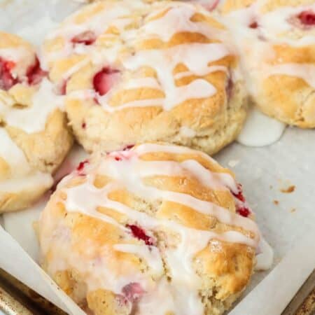 Several fresh strawberry biscuits, made with Bisquick and topped with glaze, on a parchment-lined baking sheet.