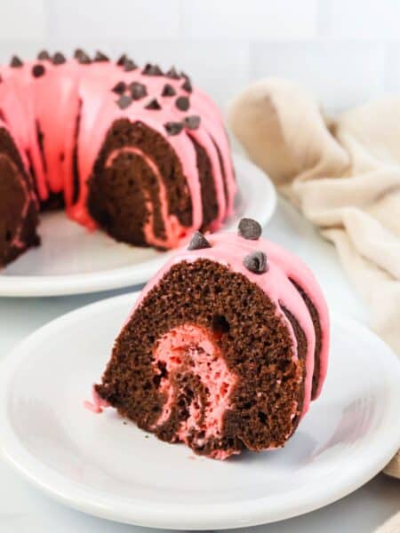 Slice of chocolate strawberry cake served on a white plate, with the remaining swirled bundt cake in the background.