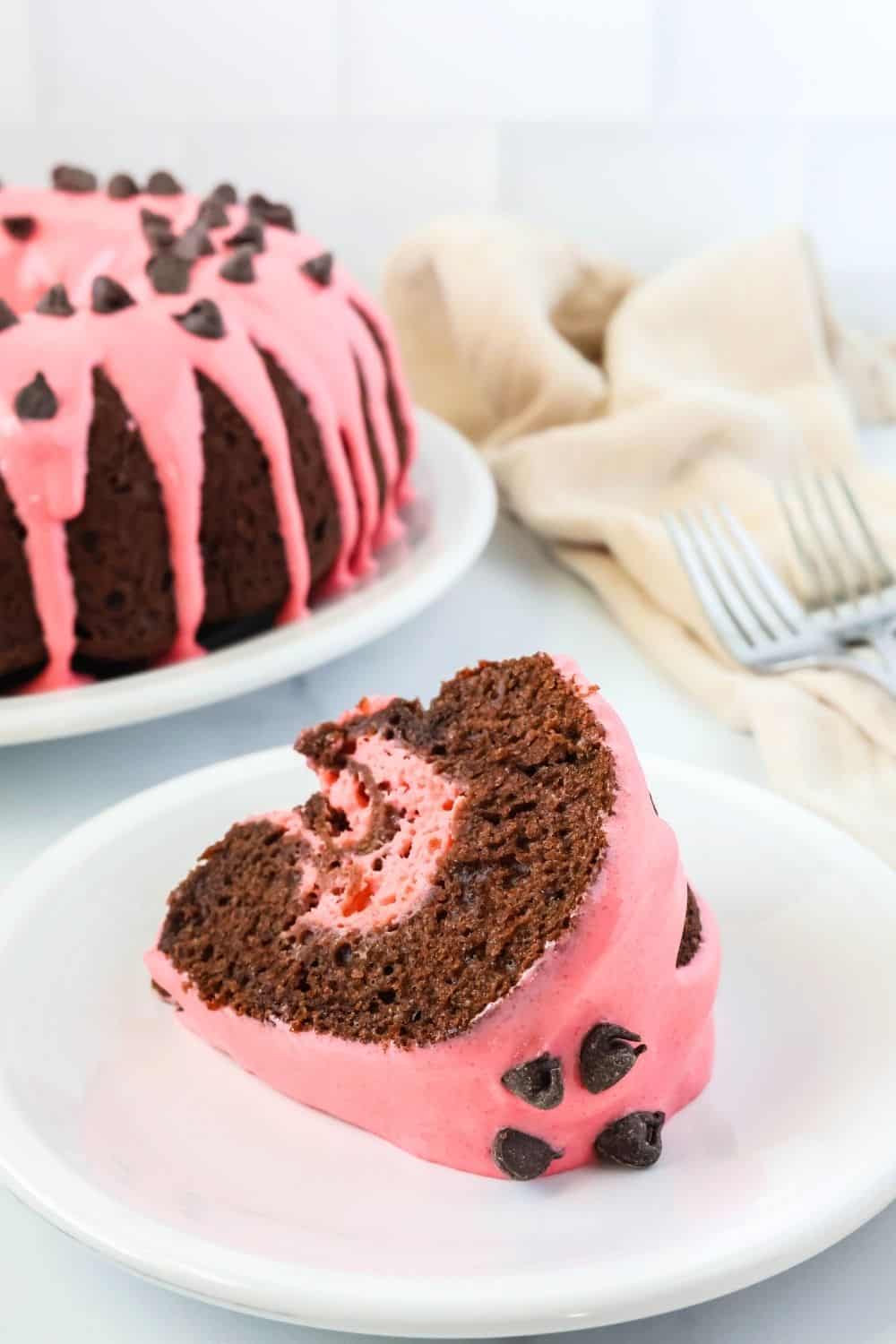 Slice of chocolate strawberry cake made from a mix, served on its side on a white plate. The remainder of the bundt cake is in the background, along with a couple of forks.