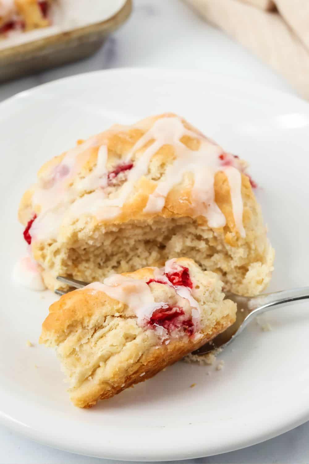 a fork cuts a bite out of a copycat Popeye's strawberry biscuit served on a white plate.
