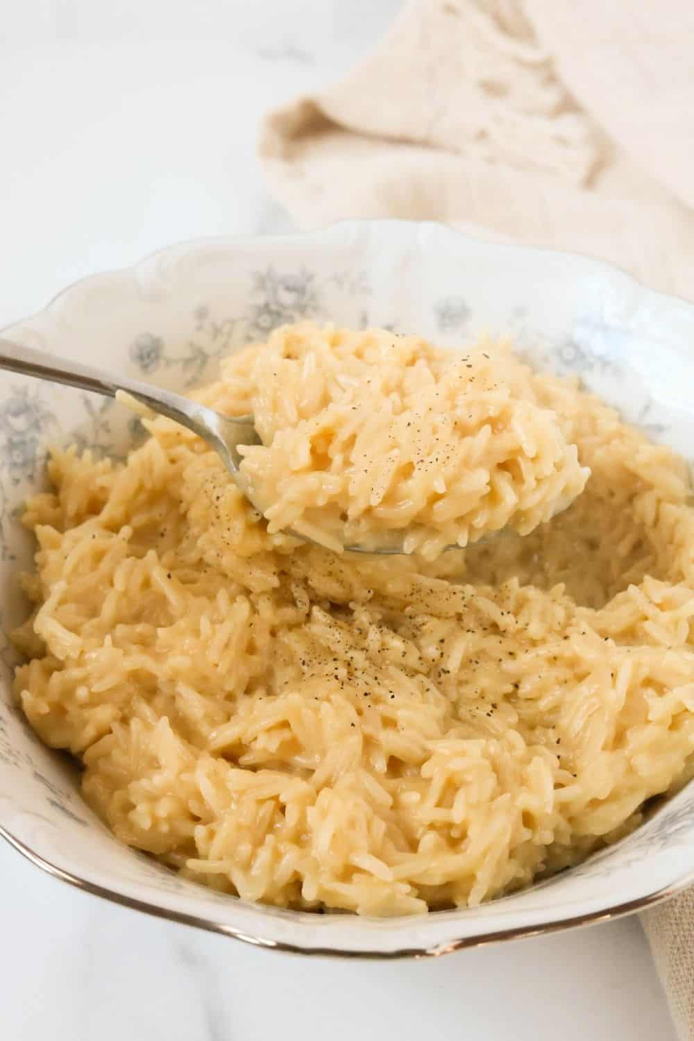 a serving spoon lifts out a scoop of cream of chicken rice from a blue and white bowl.