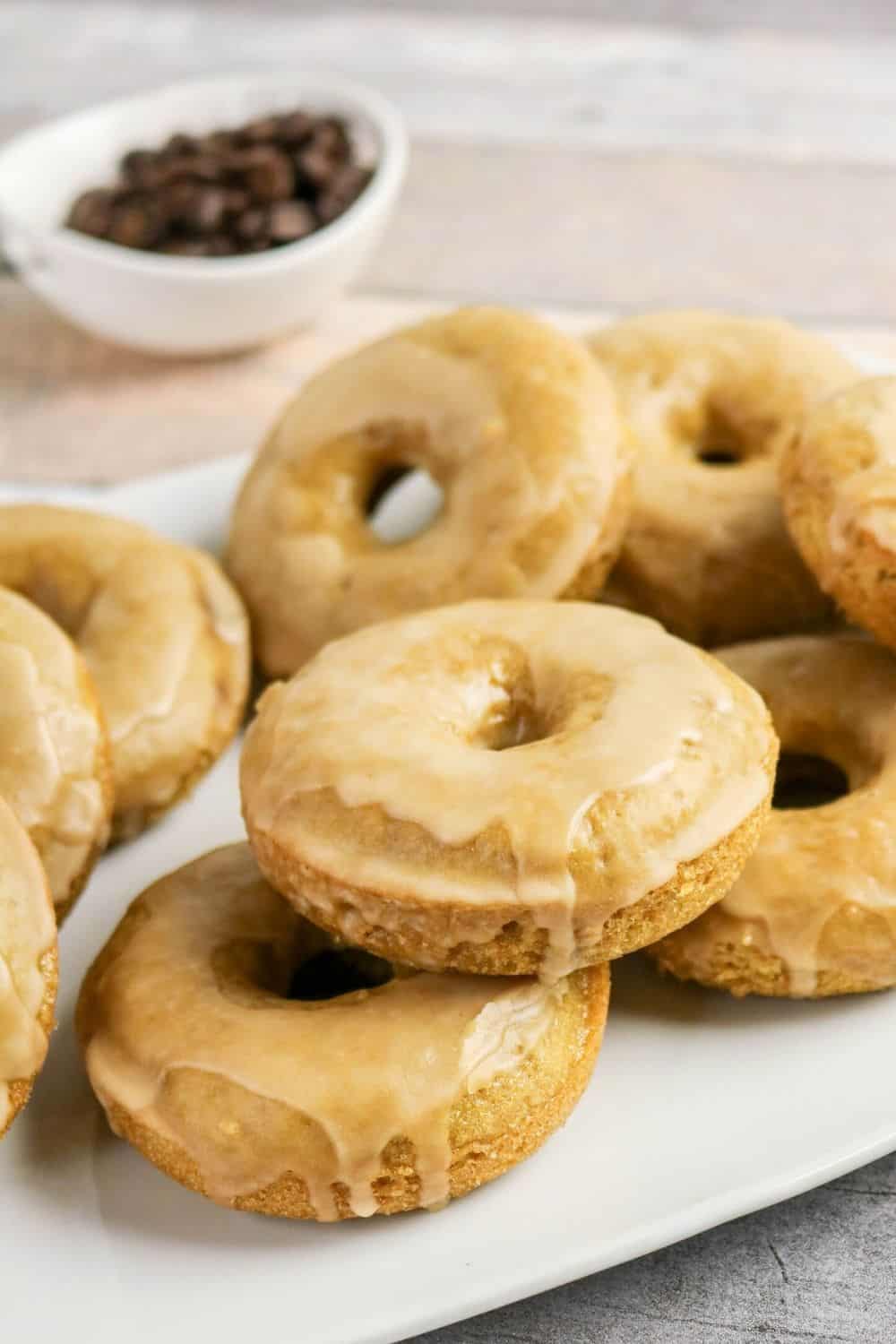 Coffee donuts served on a white platter with a bowl of coffee beans in the background.