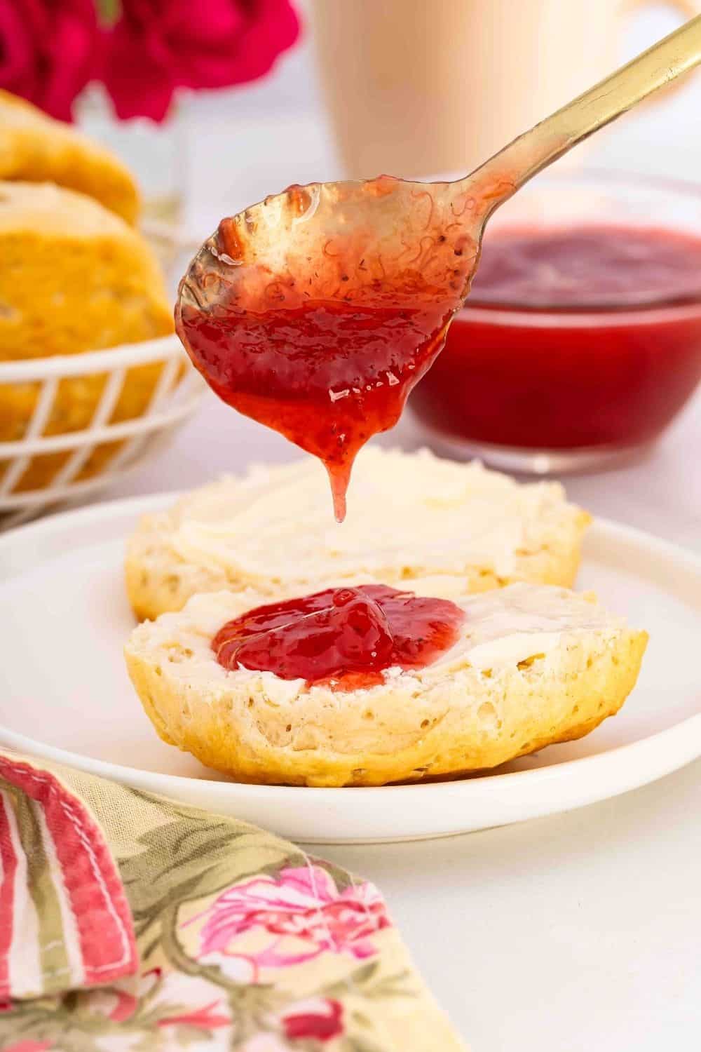 A spoon spreads strawberry rhubarb jam over a split biscuit.