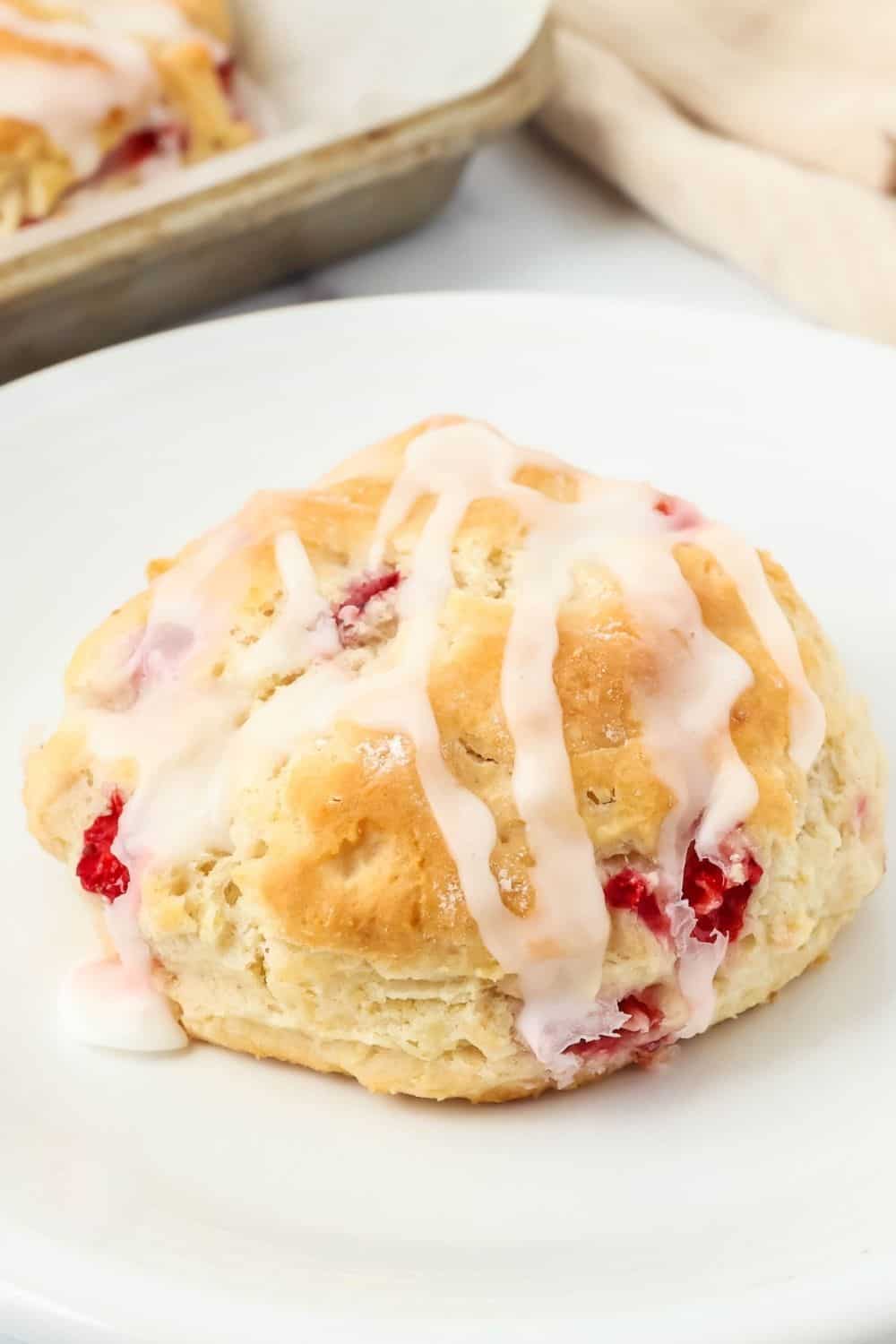 close-up view of an iced strawberry biscuit, similar to Popeye's, on a white plate.