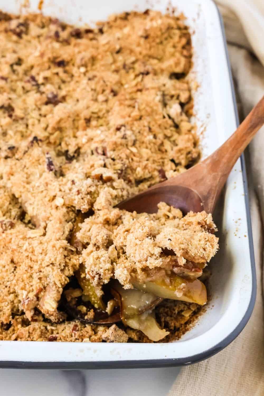 A wooden spoon scoops out a serving of pear crisp cobbler that's freshly baked in a 9x13" pan.