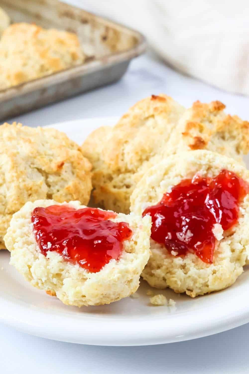 Close-up view of southern drop biscuits made with Bisquick, served on a white plate, a couple of which are topped with strawberry jam.