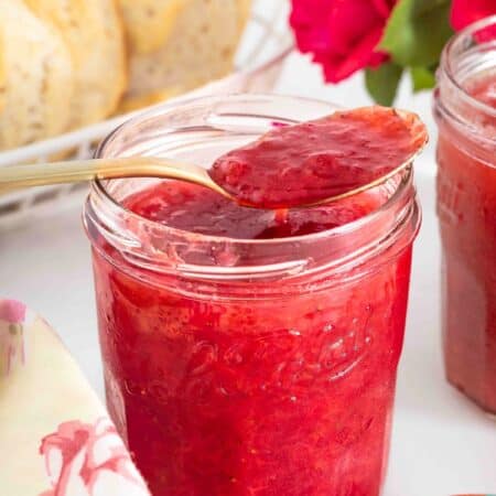 a jar of strawberry rhubarb jam with a spoon scooping out some of the jam.