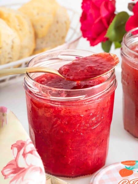 a jar of strawberry rhubarb jam with a spoon scooping out some of the jam.
