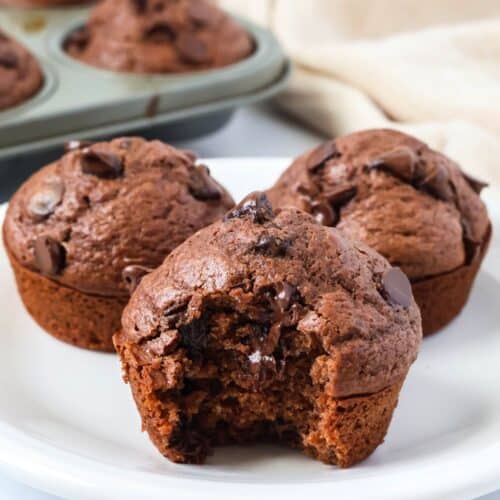 Bisquick chocolate muffins served on a white plate. One muffin has a bite taken out of it.