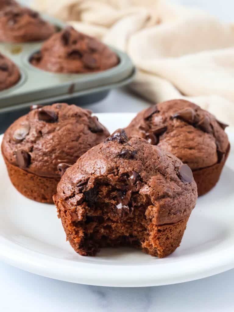 Bisquick chocolate muffins served on a white plate. One muffin has a bite taken out of it.