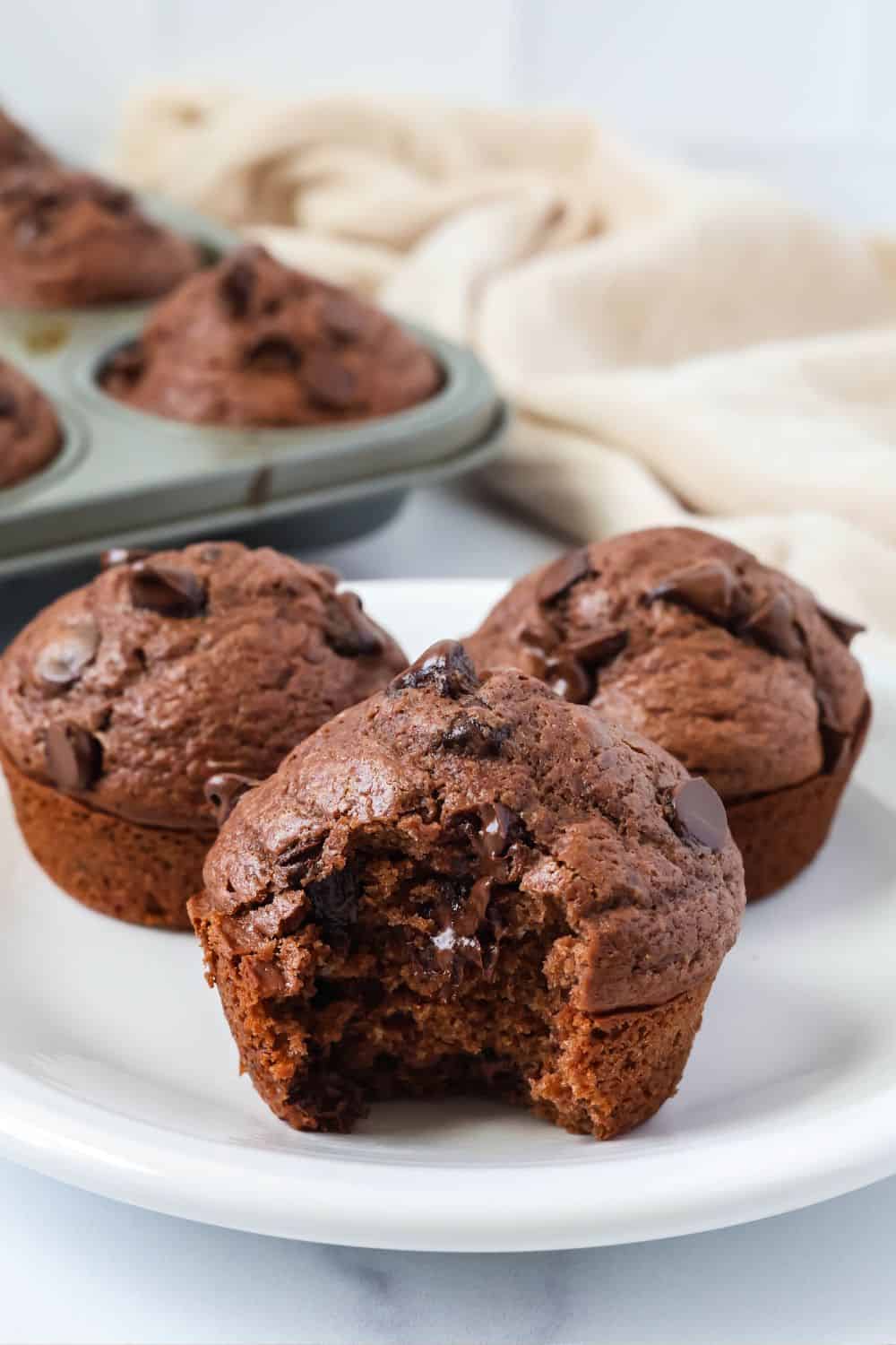 Bisquick chocolate muffins with chocolate chips served on a white plate. One muffin has a bite taken out of it.
