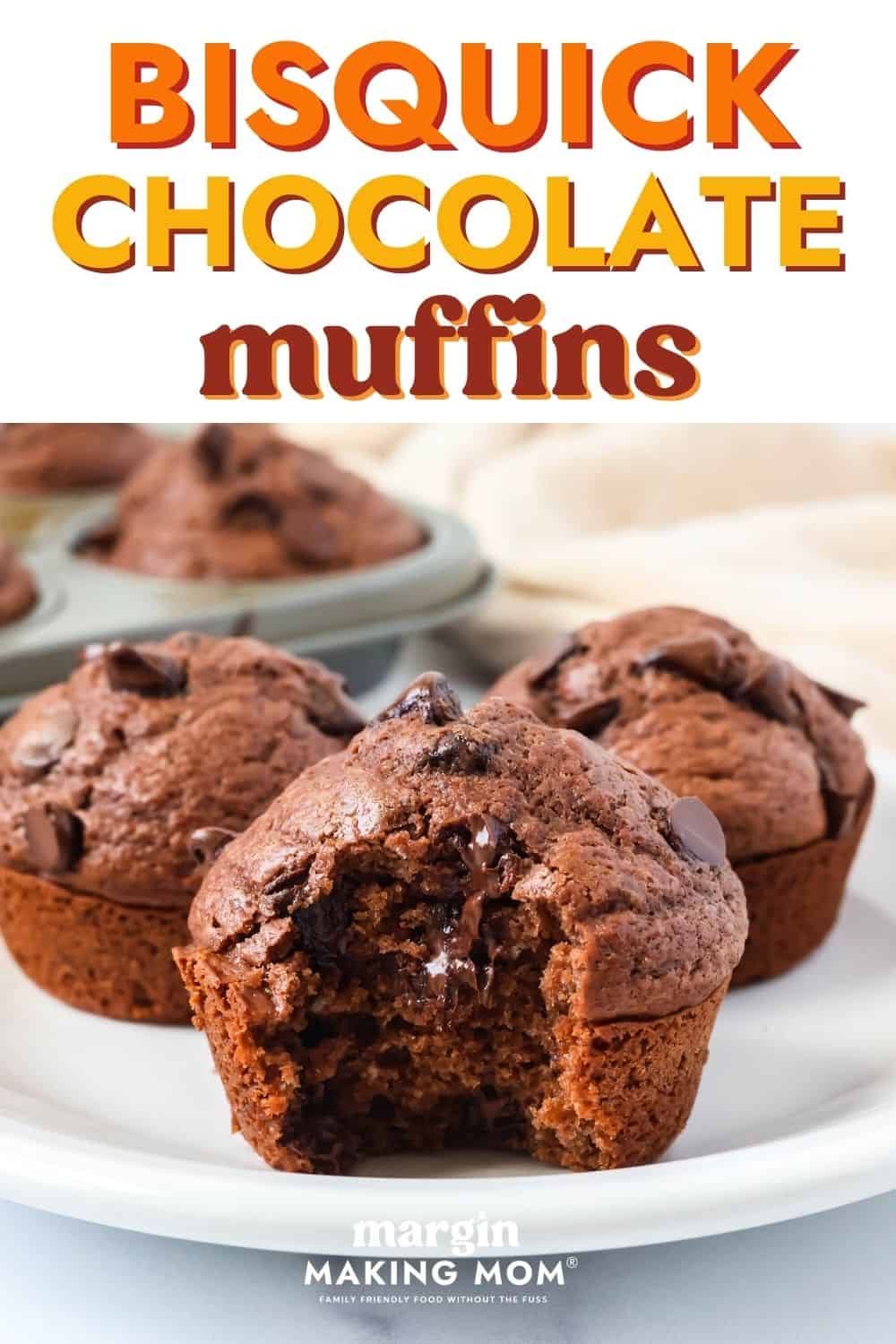 Three Bisquick chocolate muffins on a white plate, one of which has a bite taken out of it, showcasing the melted chocolate chips inside of the chocolate muffin.