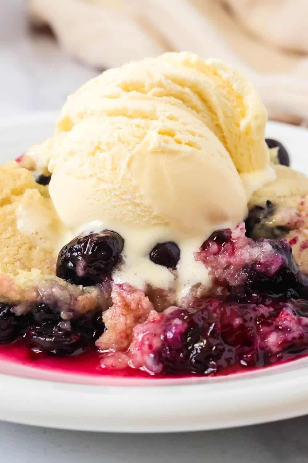 Close-up view of Bisquick cobbler made with fresh blueberries, topped with ice cream. The ice cream is melting down into the warm cobbler.