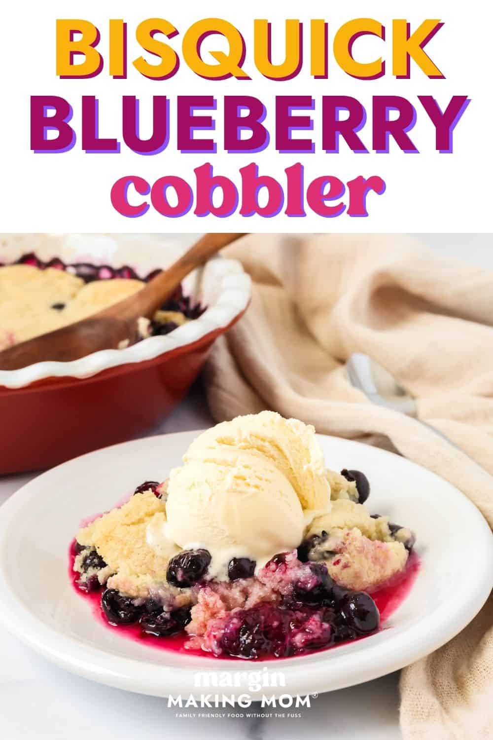Serving of Bisquick blueberry cobbler on a white plate, topped with a scoop of vanilla ice cream. The baking dish of cobbler is in the background.