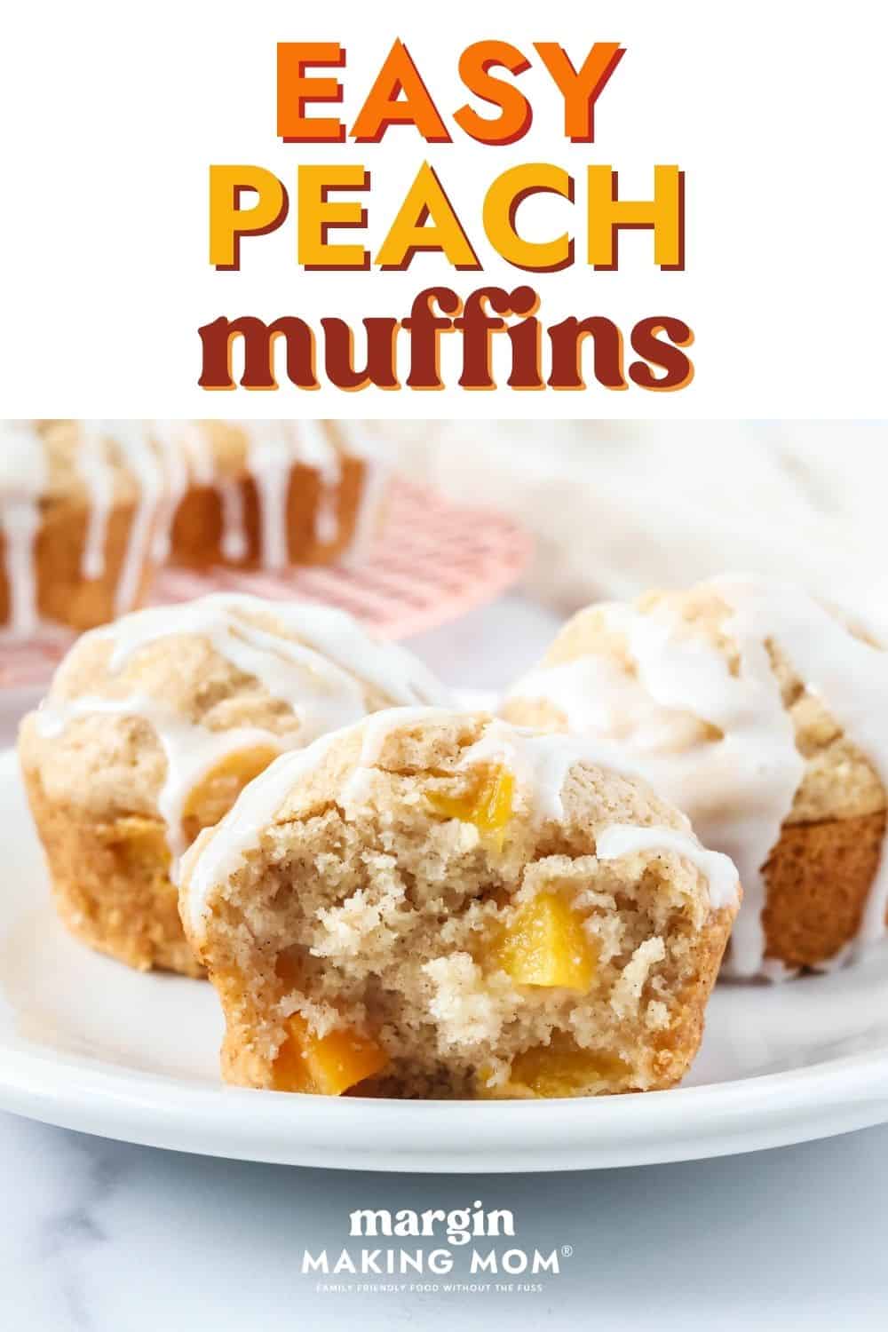 Three iced peach muffins on a white plate. One muffin has a bite taken out of it, so you can see the chunks of diced peaches in the fluffy muffin.