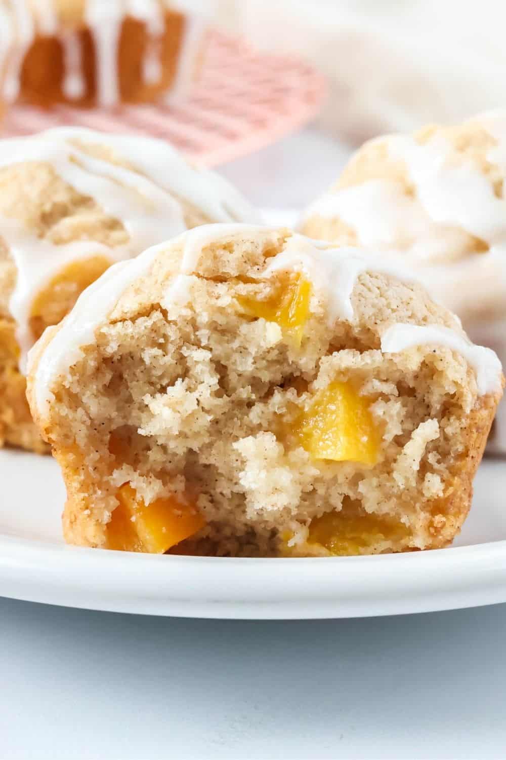 Close-up view of a fluffy peach muffin that's been torn in half, showingchunks of sweet peaches in the muffin.