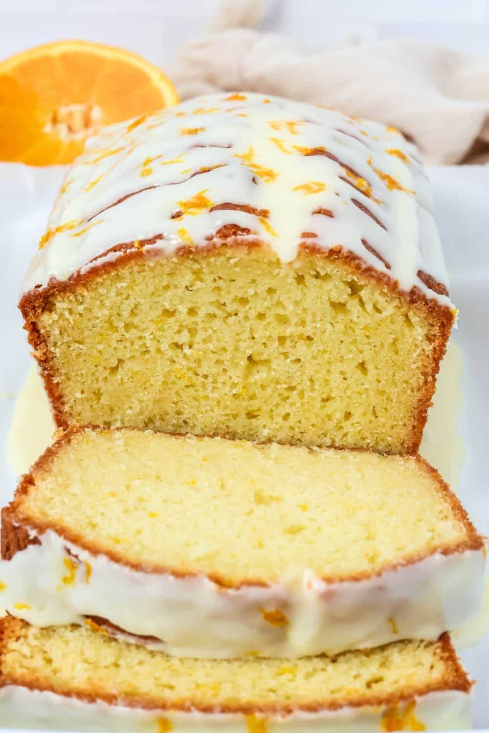 close-up view of a glazed orange loaf cake with a couple of slices cut out of it, showing the moist and tender interior crumb.