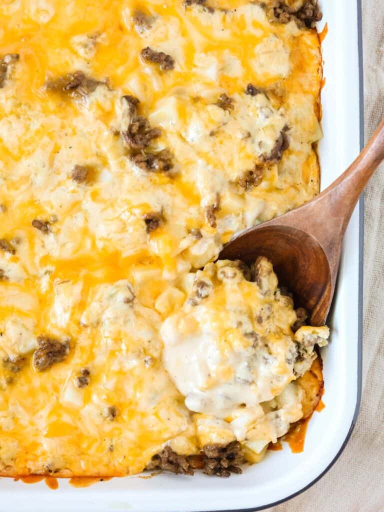 Baking dish of hobo casserole with a wooden spoon scooping out a serving.