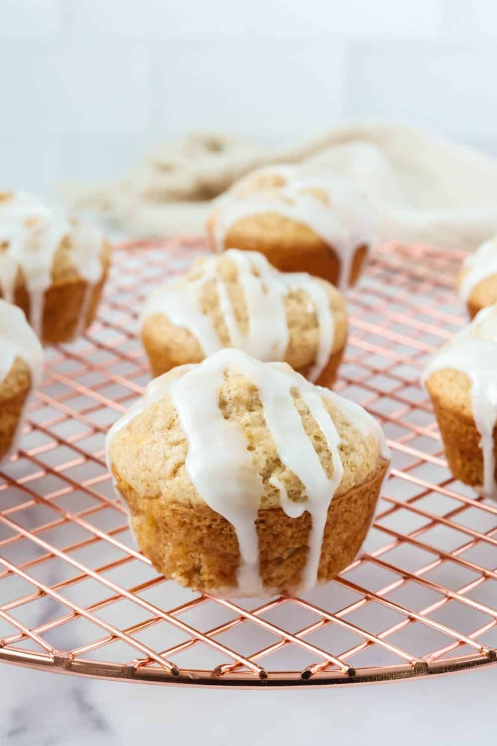 Several moist peach muffins, topped with icing, on a wire cooling rack.
