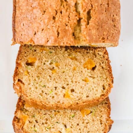 Peach zucchini loaf on a white platter, partially sliced, showing the moist interior of the bread dotted with zucchini pieces and diced peaches.
