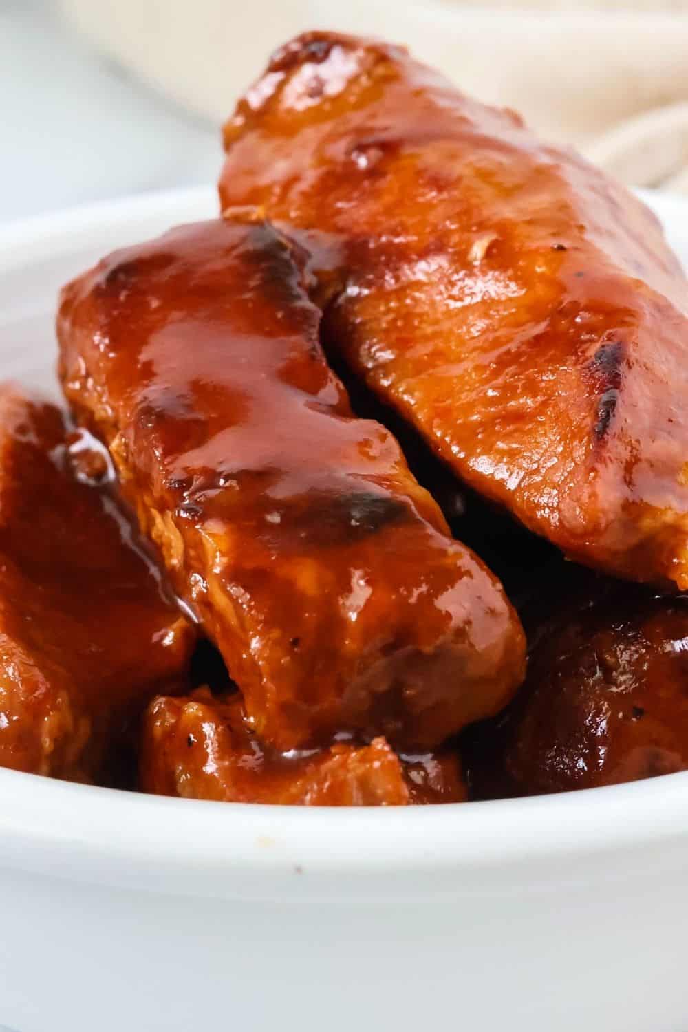 Pressure cooker boneless ribs coated in BBQ sauce, served in a white bowl.