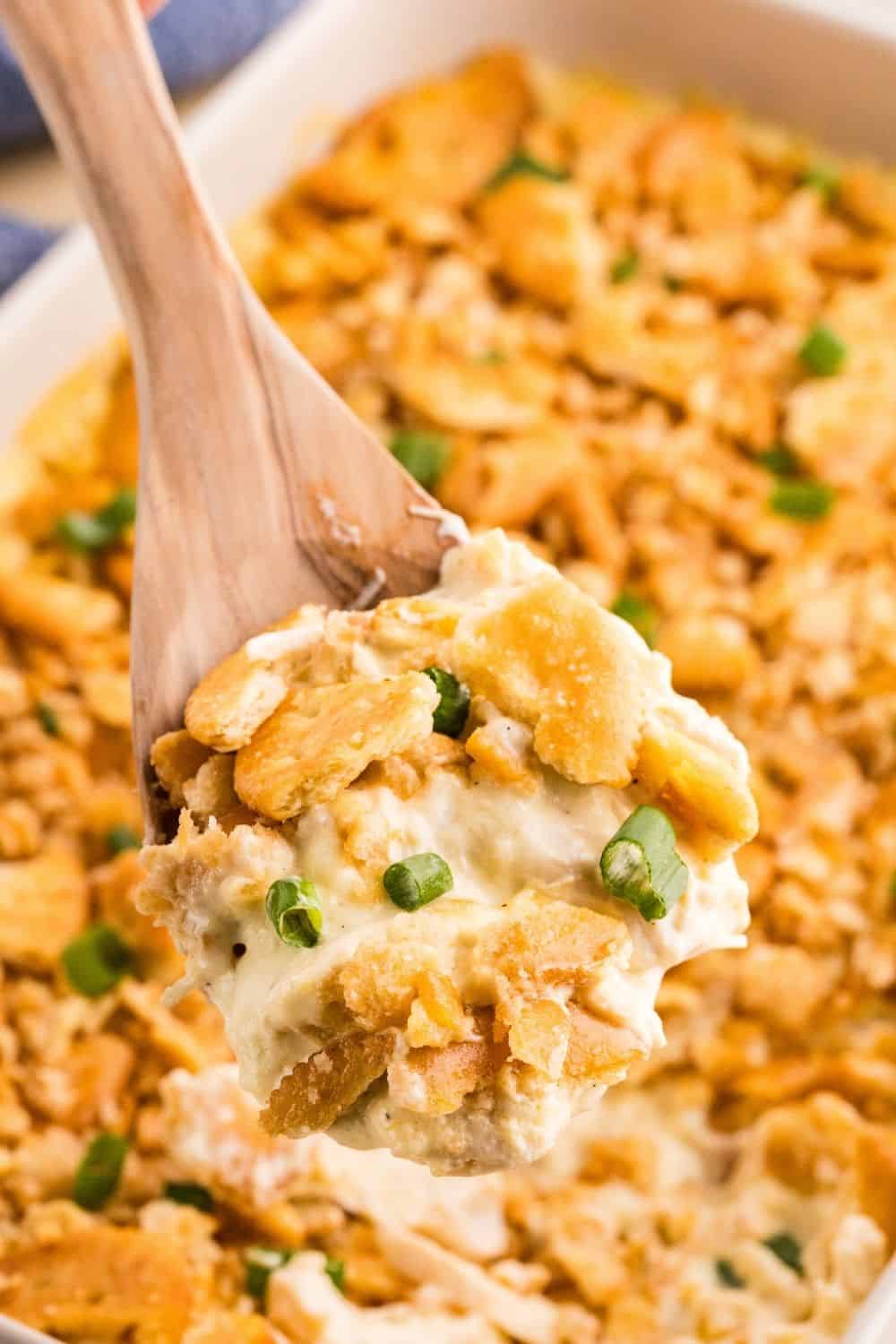 A serving spoon scoops Ritz cracker chicken from a casserole dish.