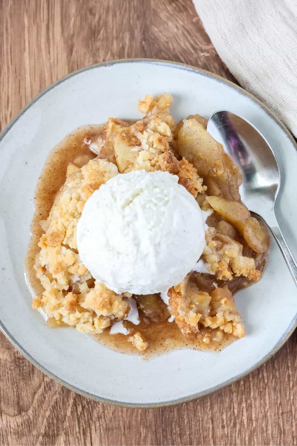 overhead view of a serving of apple crisp made with Bisquick, topped with a scoop of ice cream on an ivory plate.