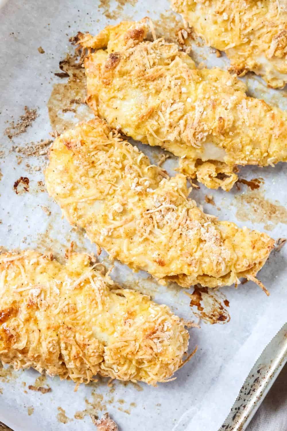 A few Bisquick chicken fingers baked on a parchment lined baking sheet.