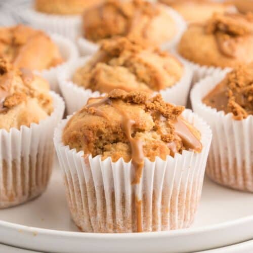 Biscoff muffins served on a white tray. Each muffin is topped with cookie pieces and a cookie butter drizzle.