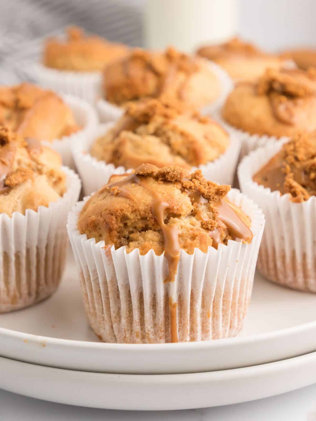 Biscoff muffins served on a white tray. Each muffin is topped with cookie pieces and a cookie butter drizzle.