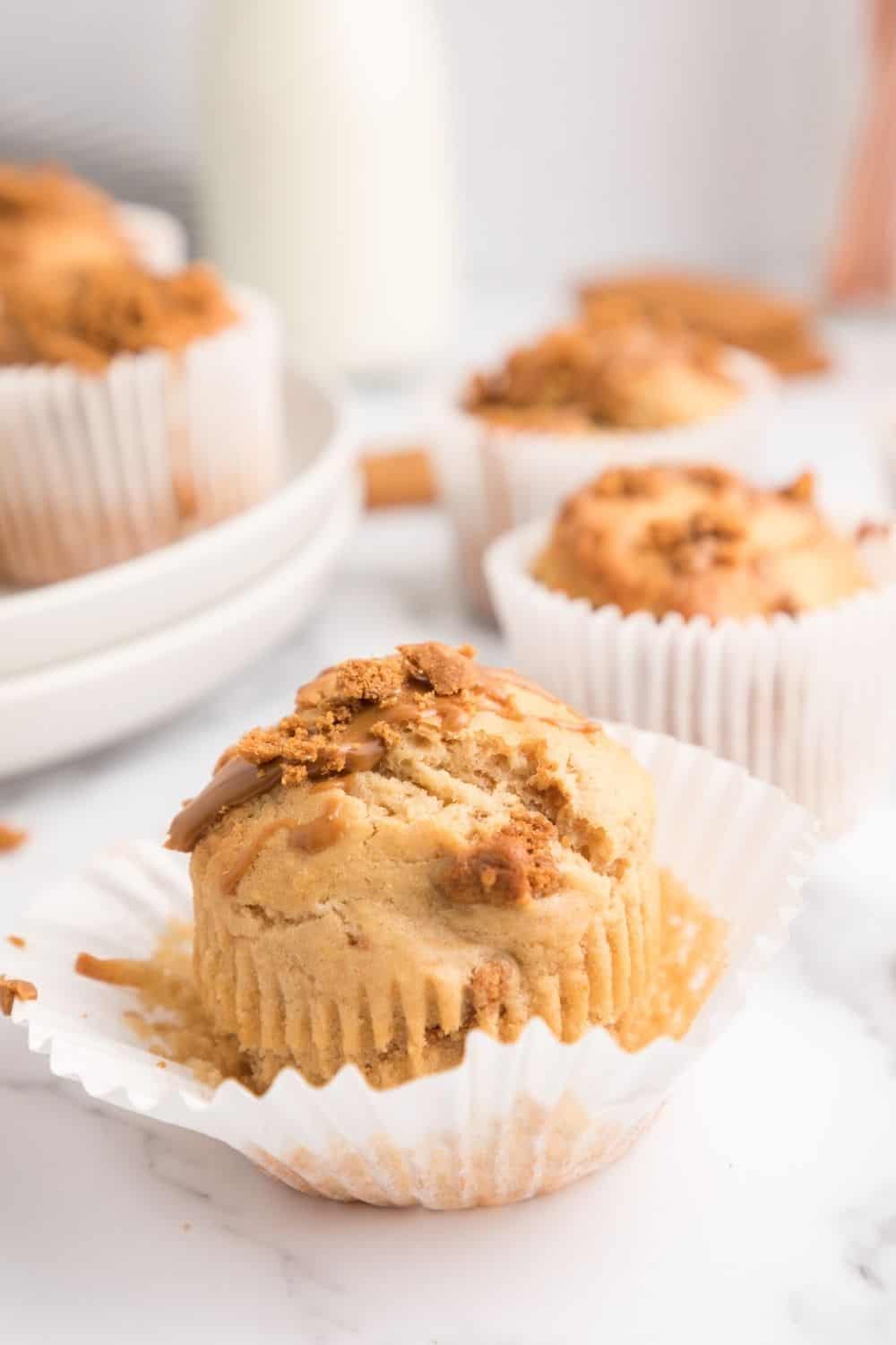 Biscoff muffin with the liner partially peeled from the muffin. Additional muffins are in the background.