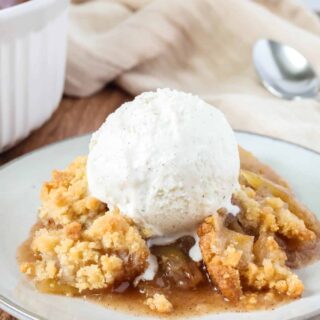 Bisquick apple crisp served on an ivory plate with a scoop of vanilla ice cream.
