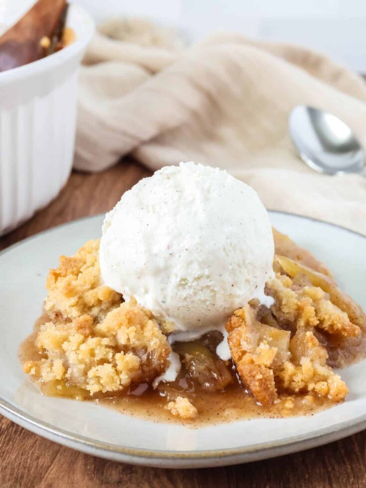 Bisquick apple crisp served on an ivory plate with a scoop of vanilla ice cream.
