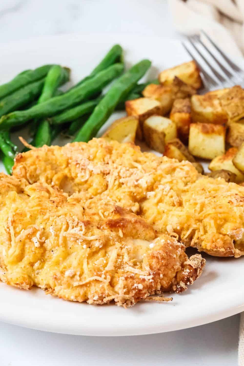 Two Bisquick baked chicken fingers on a white plate with roasted potatoes and green beans.