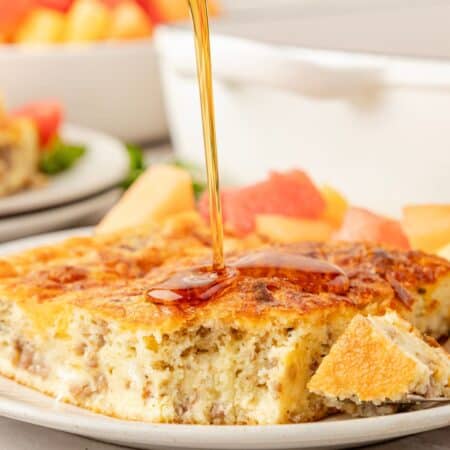 Bisquick breakfast casserole slice served on a white plate, drizzled with maple syrup.